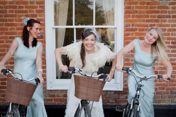 Wedding DJ at Stoke Place wedding venue in Buckinghamshire - bride and bridesmaids on bicycles