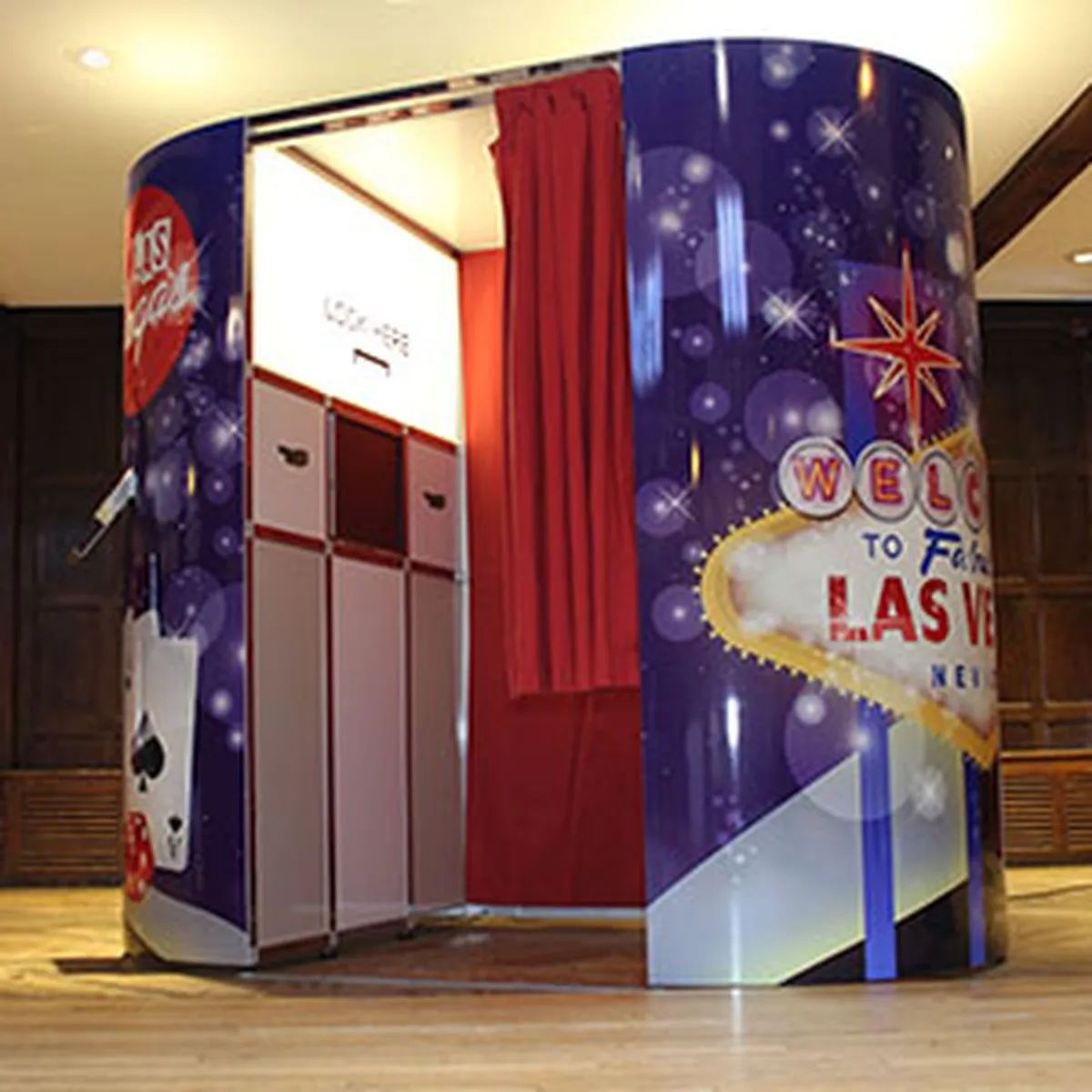 A Las Vegas-themed photo booth with a colourful exterior featuring playing cards and a Welcome to Las Vegas sign, red curtains partially open, and an inviting photo booth interior visible.