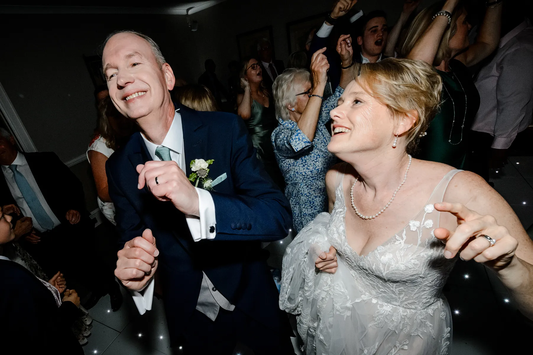 A joyful bride and groom smile and dance together at their wedding reception at Cliveden House, with guests celebrating on the dance floor thanks to an incredible wedding DJ Buckinghamshire experience.